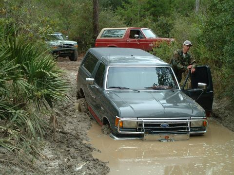 1995 Ford Bronco - Three Ford Broncos navigate a muddy trail, with one vehicle deeply stuck.