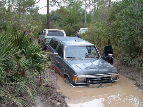 1995 Ford Bronco - Two Ford Broncos navigate a muddy trail, with one vehicle deeply stuck in the mire.