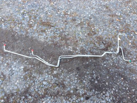 1979 Ford Bronco - A set of silver metal brake lines with red and green caps are laid out on a gravel and dirt surface.