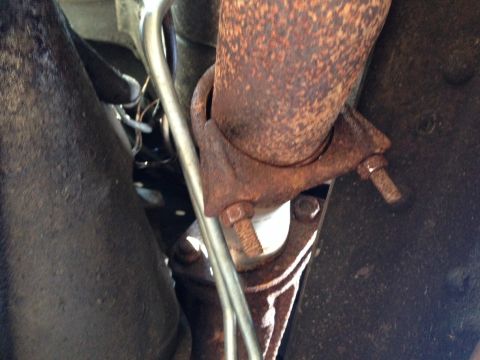 1979 Ford Bronco - A close-up view of a heavily rusted exhaust pipe and its mounting bracket, attached to a vehicle's undercarriage. A silver metal tube runs…
