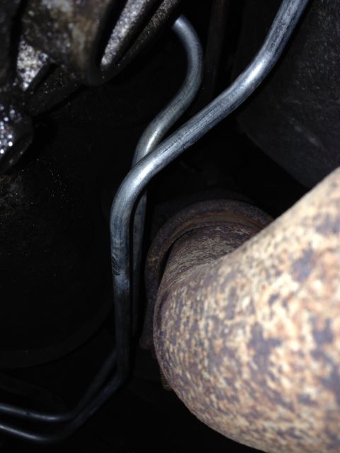 1979 Ford Bronco - Two silver metal brake lines are routed near a rusty exhaust pipe under a vehicle. The brake lines appear to be in good condition with no v…