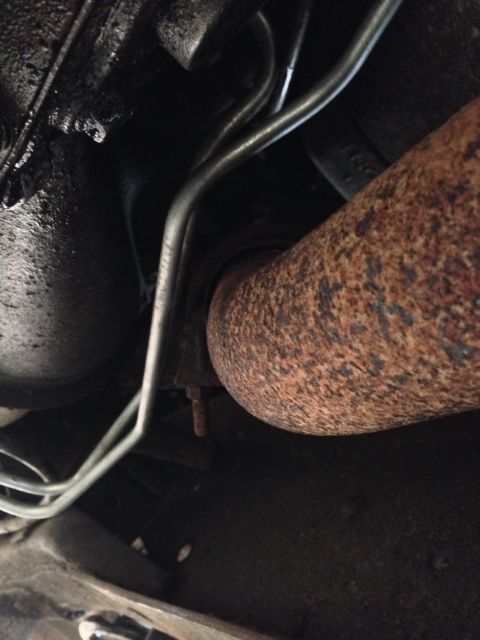 1979 Ford Bronco - This is an underside view of a vehicle's exhaust system, showing a rusted exhaust pipe and metal lines. The engine block appears to be cove…