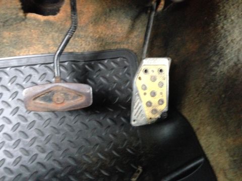 1979 Ford Bronco - Close-up view of the driver's side footwell of a vehicle, showing the clutch and brake pedals. The pedals are mounted on a black diamond pl…