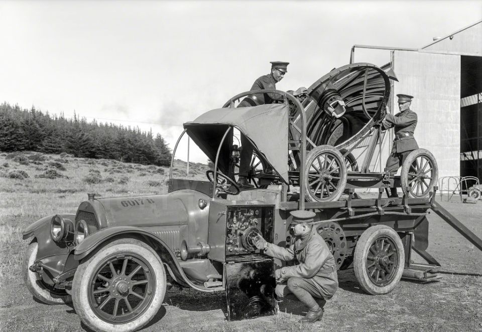 Men in uniforms operating a large dish-mounted apparatus on a truck.