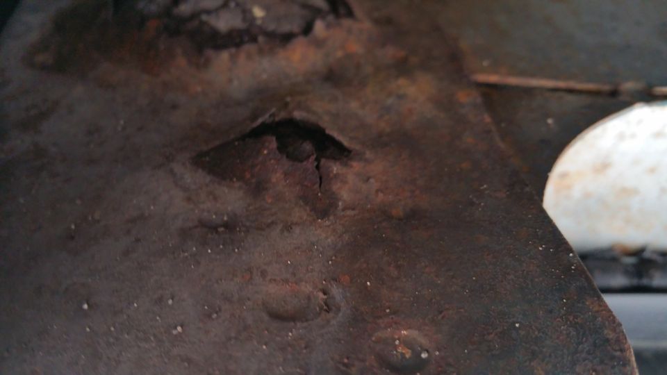 Close-up of rusted metal with a hole, possibly from a vehicle.
