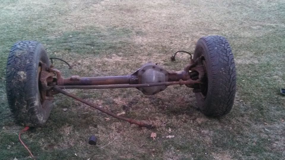 Rear axle assembly with tires from a vintage vehicle on grass.