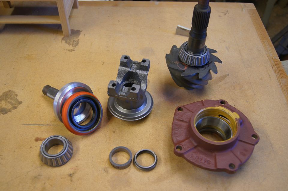 Differential parts including ring gear, pinion, yoke, seal, and bearings on a wooden surface.