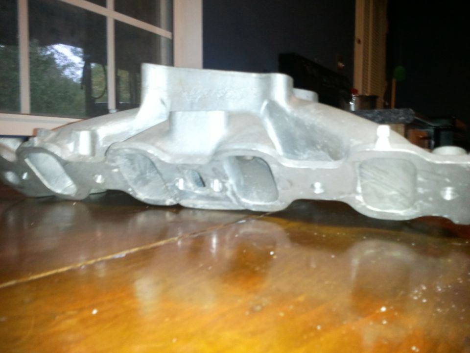 Aluminum V8 intake manifold with multiple ports on a wooden surface.