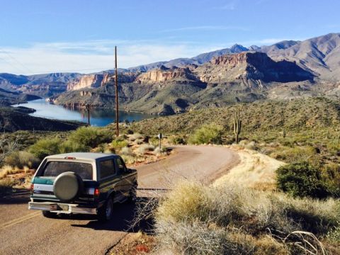 1996 Ford Bronco - A dark green and silver 1996 Ford Bronco is parked on a winding road overlooking a large lake and mountainous desert landscape.