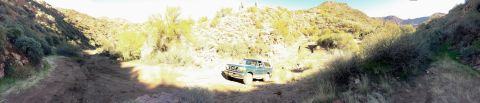 1996 Ford Bronco - A green 1996 Ford Bronco is driving on a dirt road through a desert canyon with sparse vegetation and rocky hillsides.