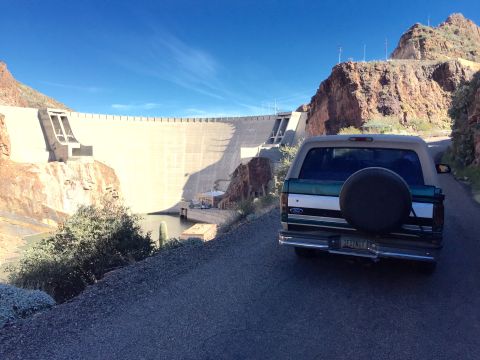 1996 Ford Bronco - The rear of a dark green and white Ford Bronco is parked on a paved road, facing away from the camera. The vehicle is positioned in front o…