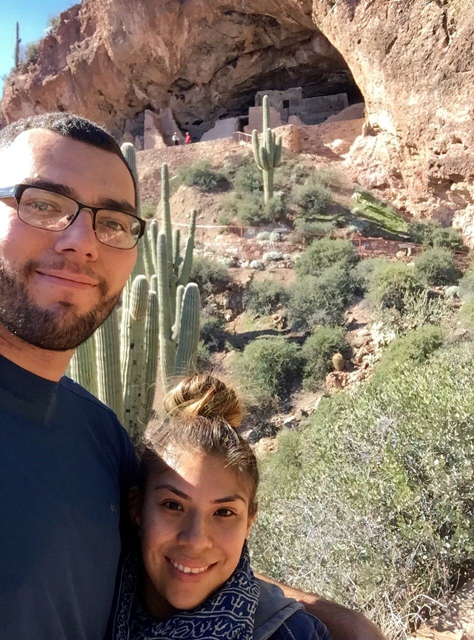 Couple taking a selfie in front of cliff dwelling and cacti.