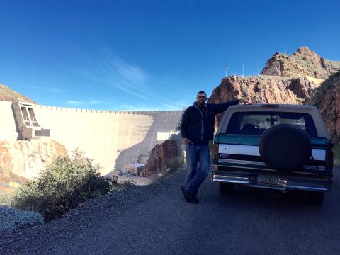 1996 Ford Bronco - A man poses next to the rear of a green and white Ford Bronco parked on a paved road in front of a large concrete dam.