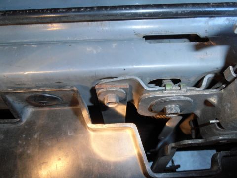 1990 Ford Bronco - Close-up view of the mounting bracket and bolts on a vehicle's frame, likely part of the hood latch or bumper assembly. The metal component…