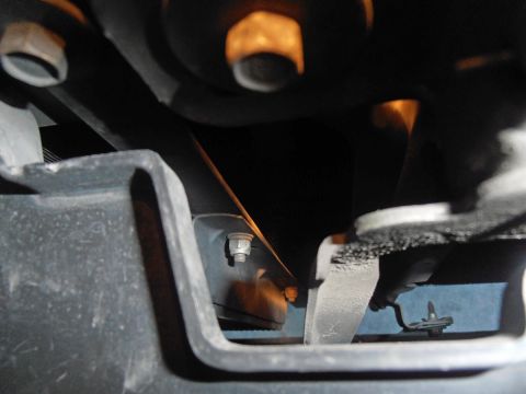 1990 Ford Bronco - A close-up view shows a bolt securing a metal bracket to a black plastic component, likely part of a vehicle's undercarriage.
