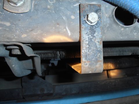 1990 Ford Bronco - A close-up view shows a rusty metal bracket bolted to a vehicle frame, with a ribbed hose or conduit visible underneath. The bracket is ang…