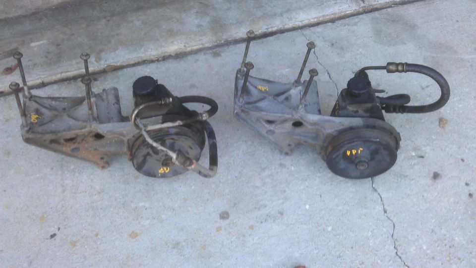 Two power steering pumps with mounting brackets on a concrete surface