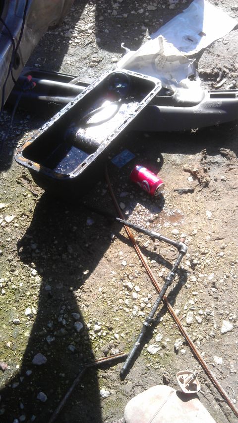 1994 Ford Bronco - An oil pan and various plumbing components are visible on the ground, alongside a discarded soda can.