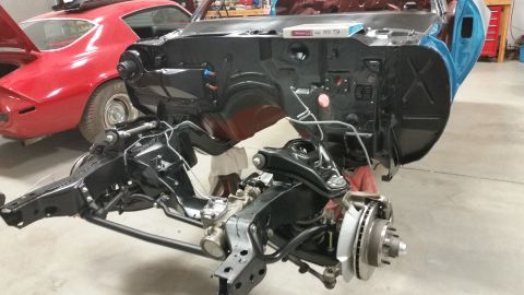 1970 Pontiac Trans Am - The front end of a car is disassembled, revealing the chassis and engine bay, with a red 1969 Chevrolet Camaro visible behind it.