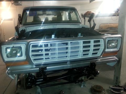 1979 Ford Bronco - Front view of a classic pickup truck undergoing restoration, with the hood up and the grille and front suspension exposed. The vehicle is l…