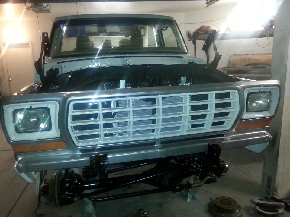 Front view of a classic gray pickup truck with hood open, showing grille and suspension.