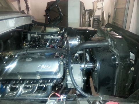 1979 Ford Bronco - The engine bay of a classic Ford Bronco is shown, featuring a V8 engine with chrome valve covers and exhaust headers. The radiator and fan…