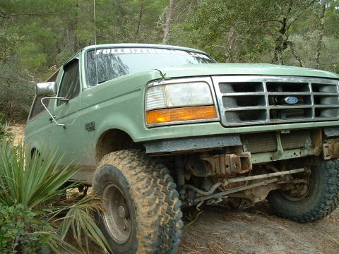 1995 Ford Bronco - This 1995 Ford Bronco is shown off-roading on a dirt trail with large, knobby tires.