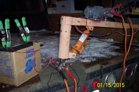 1973 Ford F-250 - A close-up view of a makeshift winch and hydraulic jack assembly connected to a battery with jumper cables, resting on a snow-covered flatb…