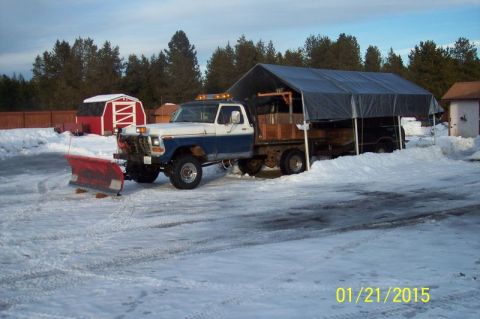 1973 Ford F-250 - A blue and white Ford F-250 pickup truck equipped with a red snow plow is parked in a snowy yard next to a tarp-covered structure. The truc…