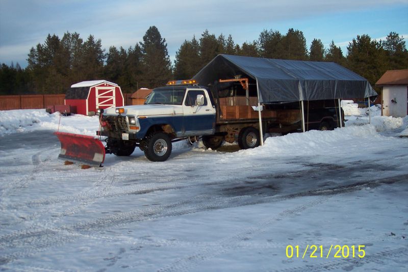 Blue and white Ford F-250 pickup truck with a red snow plow in a snowy yard.