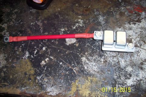 1973 Ford F-250 - A red battery cable with a ring terminal on one end is connected to a two-fuse block assembly with two bolts. The assembly is mounted on a…