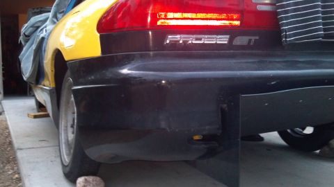 1995 Ford Probe - The rear driver's side quarter panel and bumper of a yellow and black Ford Probe GT are shown. The car is parked on a concrete surface with…