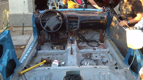 1995 Ford Probe - The interior of a disassembled blue car is shown, with the dashboard, steering wheel, and exposed wiring visible. Tools and a large plastic…