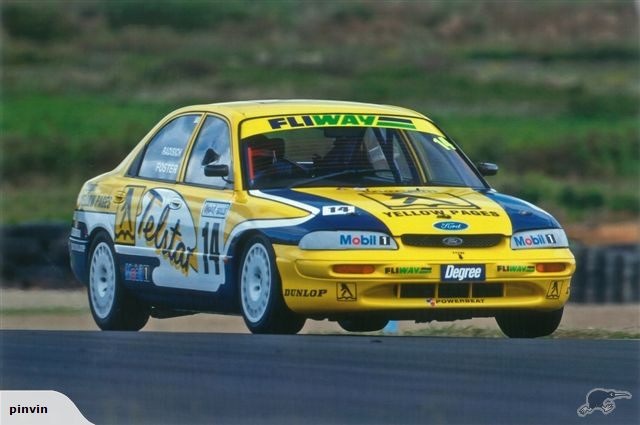 Yellow and blue Ford sedan race car with number 14 and sponsor decals on a race track.