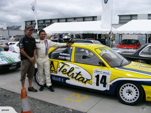 1993 Mazda MX-3 - Two men stand next to a yellow and blue race car with "Telstar" branding and the number 14 on its side.