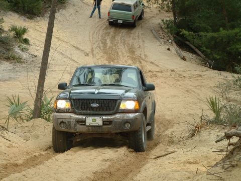 1995 Ford Bronco - Two Ford SUVs, a Ranger and a Bronco, navigate a sandy incline on an off-road trail.