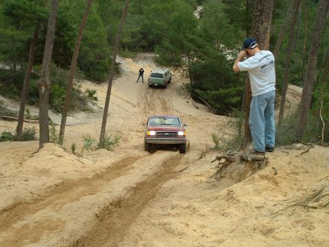 1995 Ford Bronco - Two vehicles navigate a sandy trail with a spectator observing the off-road action.