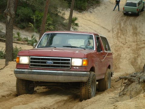 1995 Ford Bronco - A red Ford Bronco navigates a sandy incline, with another SUV visible further up the hill.