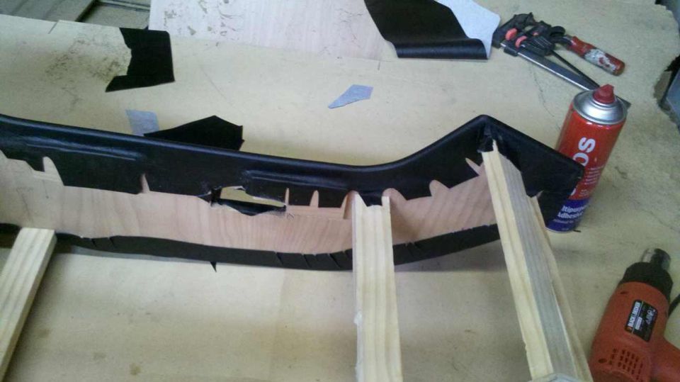 Black car interior trim piece with wood backing, being worked on with tools and spray can