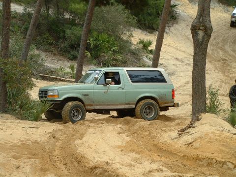 1995 Ford Bronco - A green 1995 Ford Bronco navigates a sandy off-road path, with another vehicle visible further up the trail.