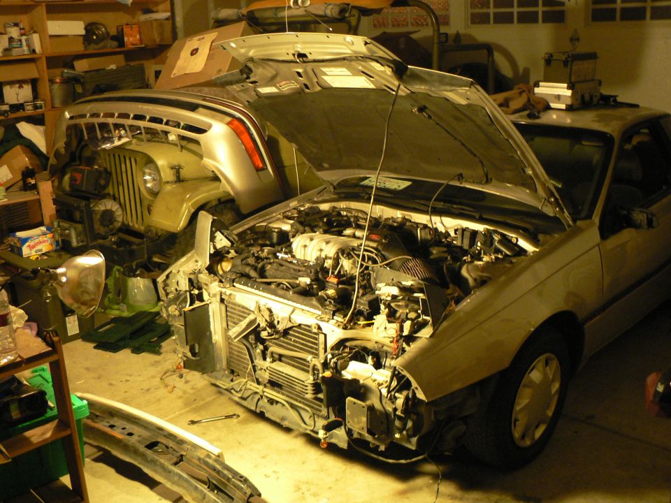 Jeep Wrangler and a sedan with hoods open in a garage, both appear to be undergoing repairs