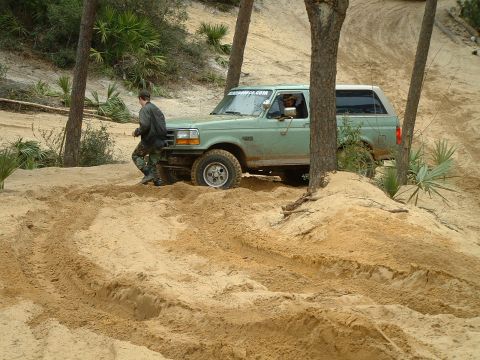 1995 Ford Bronco - A 1995 Ford Bronco navigates sandy terrain, with a person walking alongside the vehicle.
