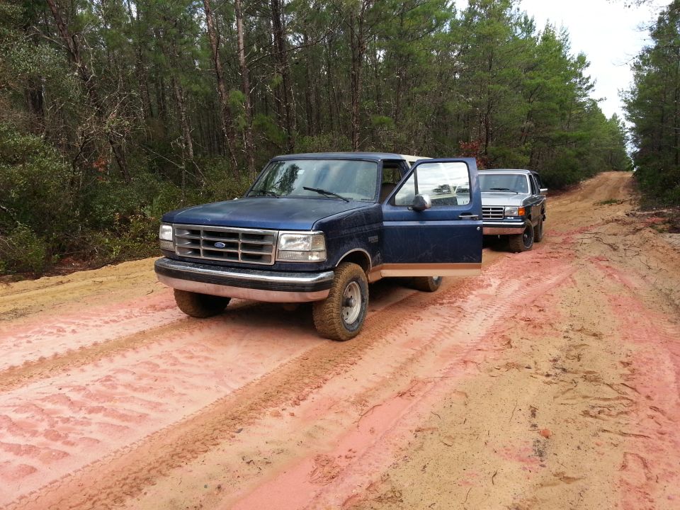 Blue Ford F-Series truck with driver's door open, parked on a dirt road