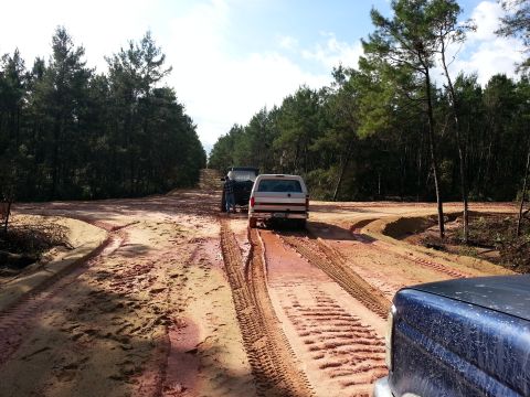 1994 Ford Bronco - Two SUVs navigate a muddy, rutted dirt road through a wooded area.