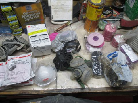 2004 Aston Martin Virage - Various respirator masks and filters are laid out on a workbench, alongside cans of solvent and wood stain.