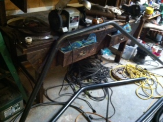 1995 Ford Bronco - Metal tubing for a roll cage lies on a workbench cluttered with tools and electrical wiring.