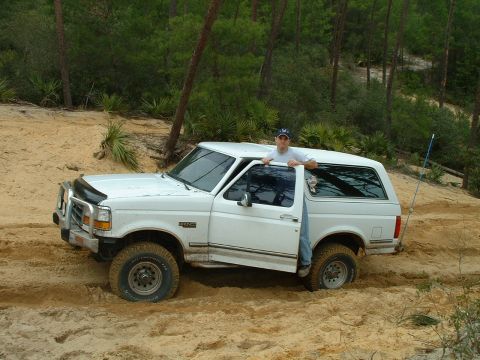 1995 Ford Bronco - White 1995 Ford Bronco is stuck in a sandy off-road area with trees in the background.