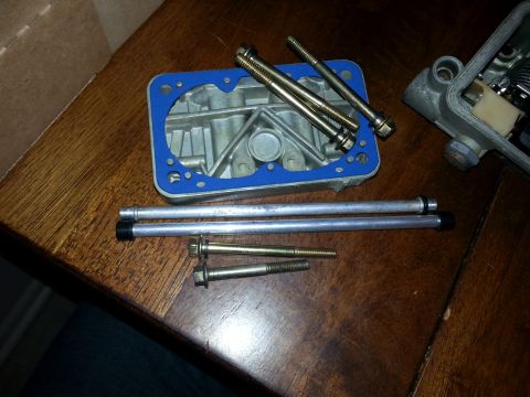 1981 Ford Bronco - Carburetor base plate, gasket, and hardware laid out on a wooden surface.
