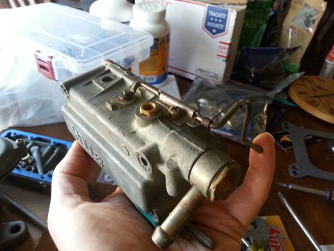 1981 Ford Bronco - A carburetor part is held in a hand, with other items on a table.