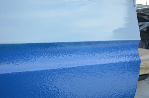 1979 Ford Bronco - A close-up view of a vehicle's painted metal panel, a textured blue lower section and a smooth light blue upper section.